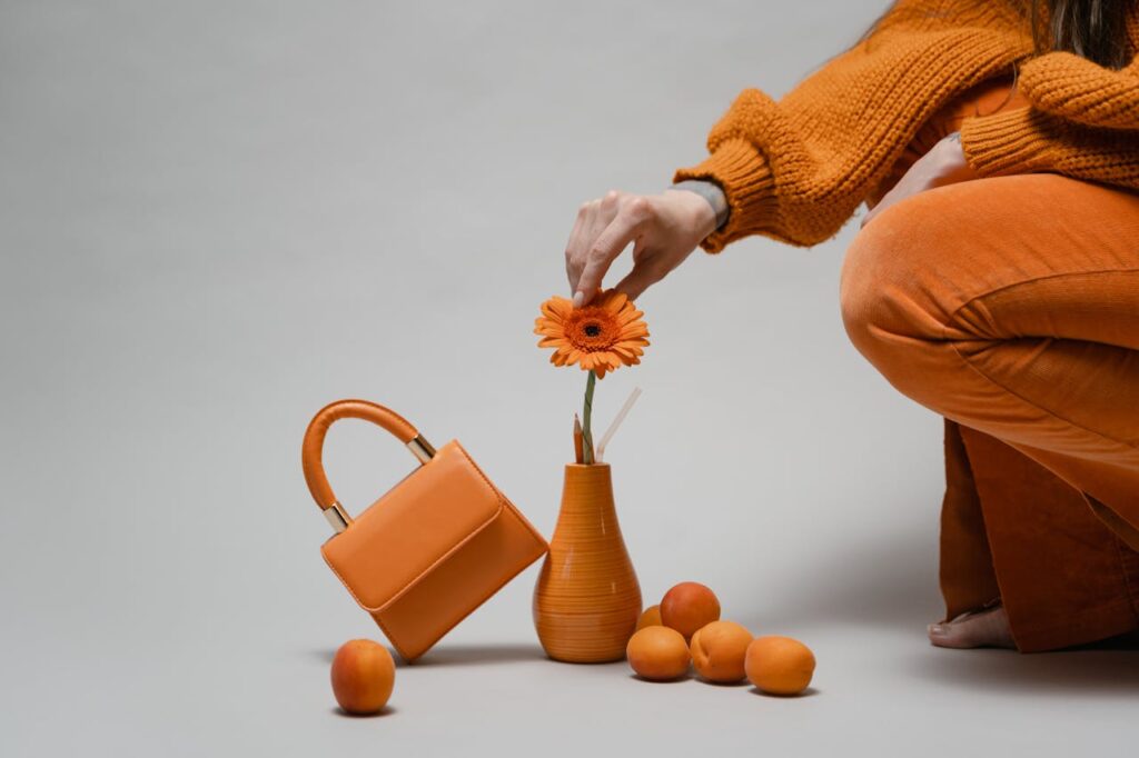 pexels-photo-8801167 A minimalist composition featuring a woman arranging an orange flower in a vase with matching accessories.
